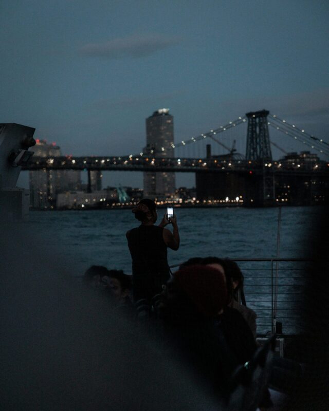 Passeggeri sul ponte del battello fotografano lo skyline di New York all'ora blu