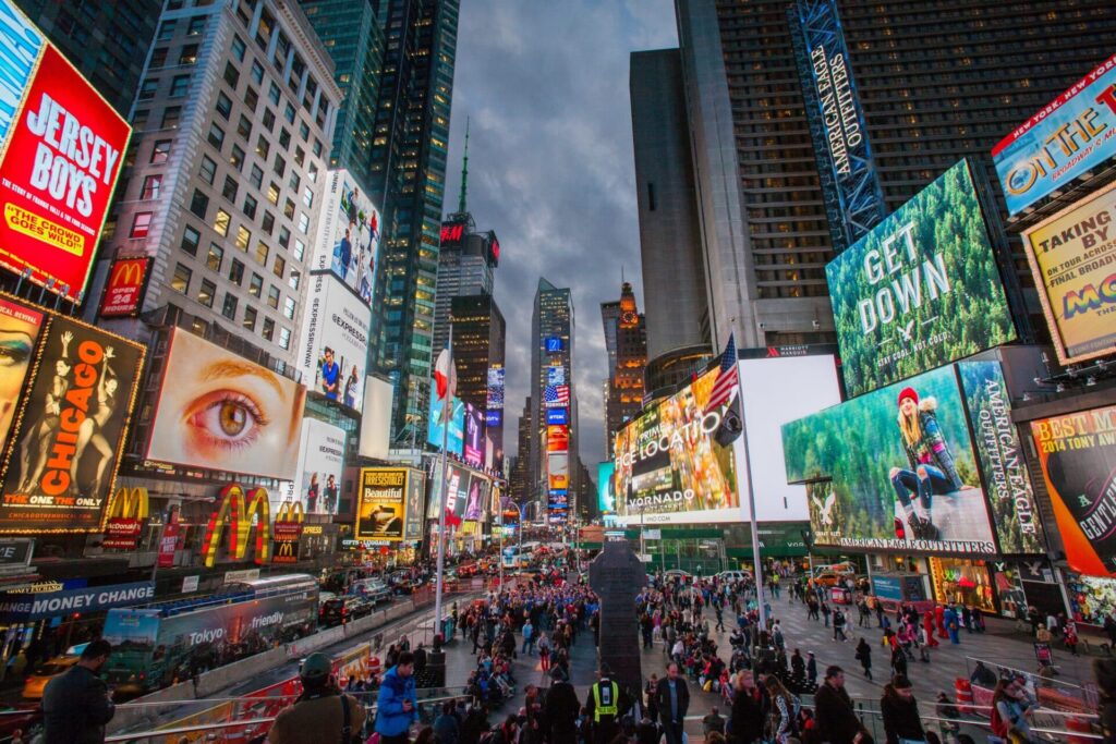 Times Square affollata al tramonto con le insegne luminose dei musical di Broadway