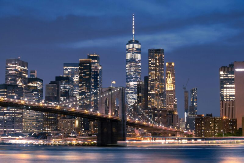 Ponte di Brooklyn e One World Trade Center illuminati visti dall'acqua di sera